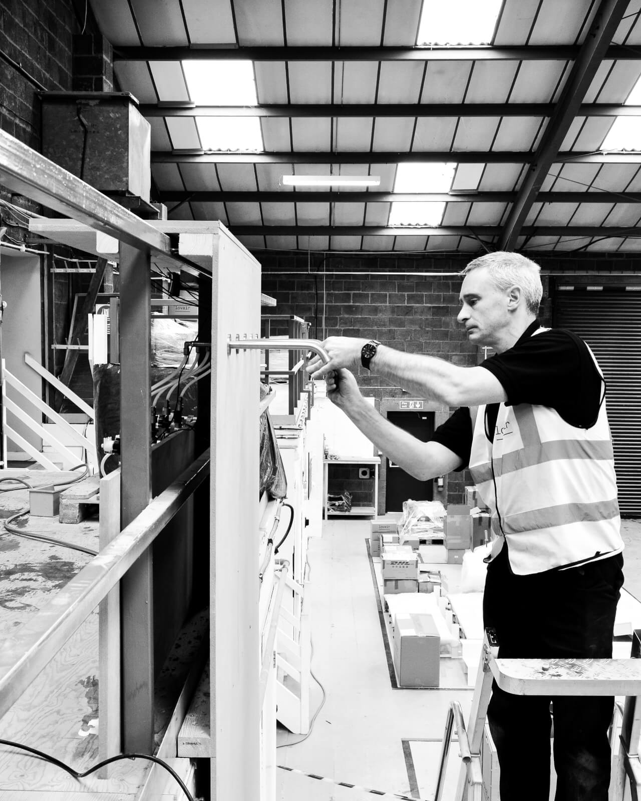 Black and white image of a Splash Lab worker adjusting a tap in their Manchester warehouse on the four-metre waterfall project featuring 5 capacitive taps